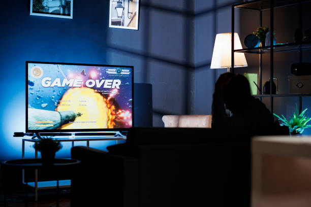 Male gamer feeling frustrated after losing shooting game contest, engaging in online multiplayer tournament late at night. Sad displeased man playing first person video games on television.