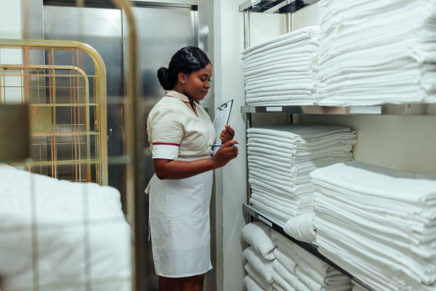 Young African-American woman in white uniform working at the hotel checking the clean bed sheets in the laundry